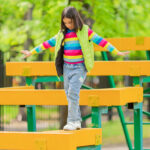 a cute little girl on a childrens playground, walks on wooden bars, keeps a balance