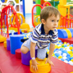 cute little boy crawling and playing on colorful playground at shopping mall.
