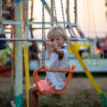 happy blonde toddler child waving at the camera riding a carouse