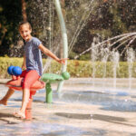 happy little girl in splashes on water playground