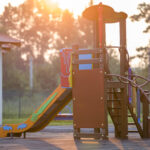 nursery playground with colorful slides on soft rubber flooring with no children at sunset or sunrise.