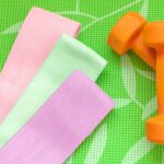 orange dumbbell for fitness and sports elastic bands on a green background, concept of home workouts