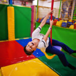 smiling boy swinging on a rope at indoor playground.