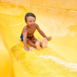 tanned joyful kid rides on a water slide, amusement attraction in the water park, children's amusement ride roller coaster.