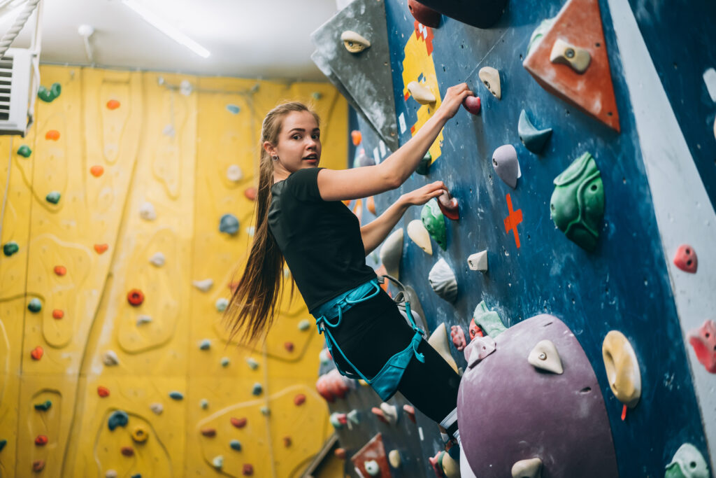 young woman climbing a tall, indoor, man made rock climbing wall
